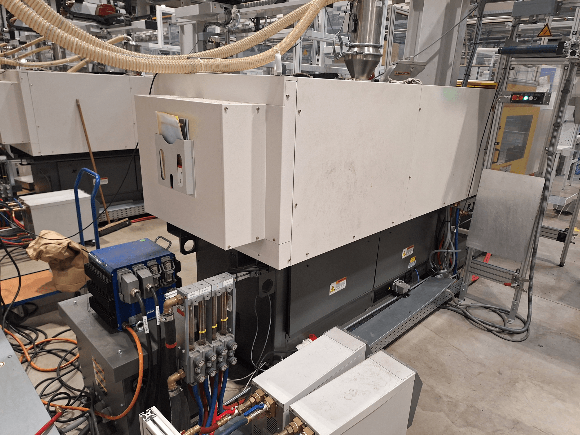 Équipement industriel dans une usine ; comprend une grande machine avec un panneau de commande, des tuyaux et des connexions électriques, vue de côté.