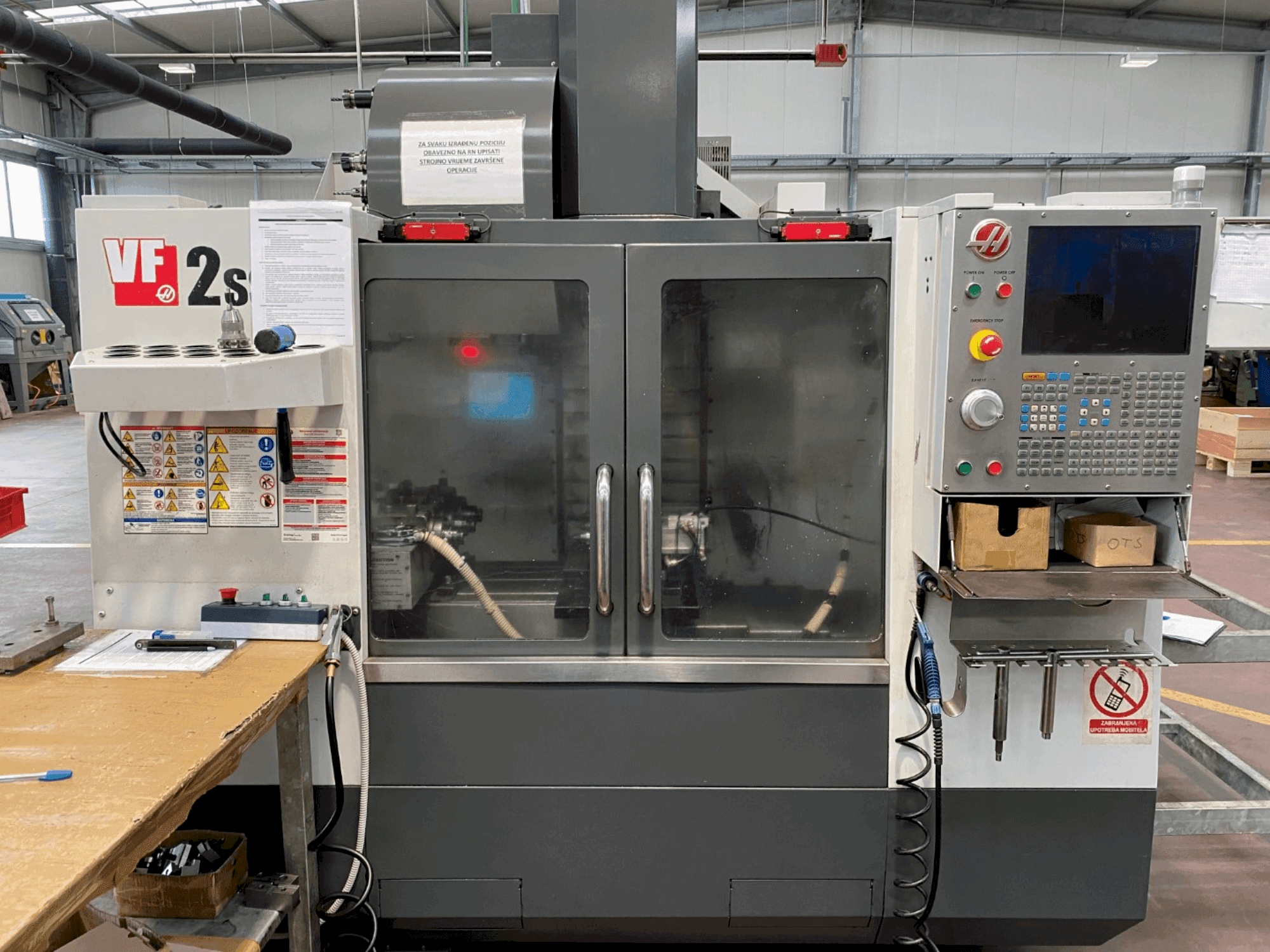 Centre d'usinage Haas VF-2SS vu de face, avec panneau de commande, tuyau d'arrosage et étiquettes de sécurité sur le côté.