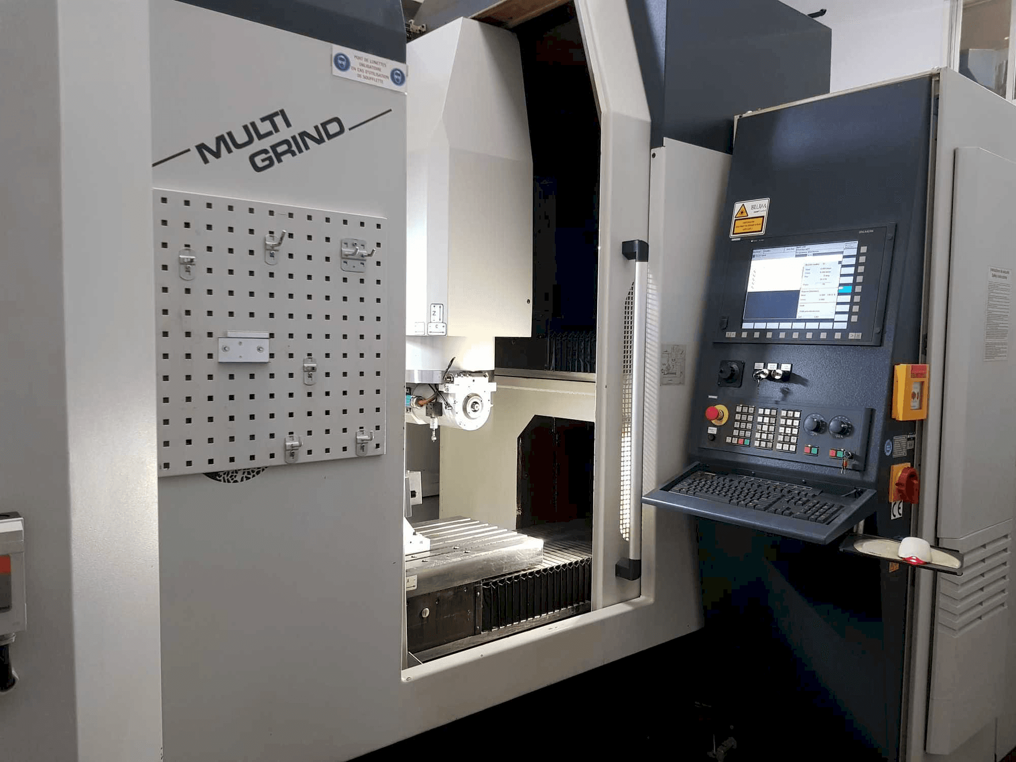 Machine CNC Multi Grind vue de face, avec un panneau de commande, un tableau de rangement et une zone de travail ouverte.